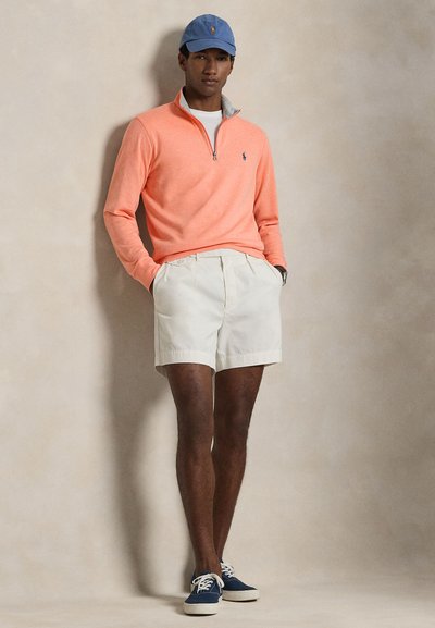 Ελαφρύ κοράλλι πουλόβερ με φερμουάρ στο γιακά· κρεμ σορτς· μπλε καπέλο με λογότυπο· ναυτικά αθλητικά παπούτσια· λεία υφή· casual γραμμή.