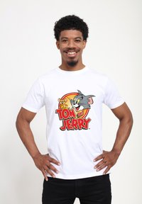 Hvid bomulds T-shirt med et farverigt grafiktryk af Tom og Jerry med en cirkulær baggrund, der fremhæver karakterernes legesyge udtryk.