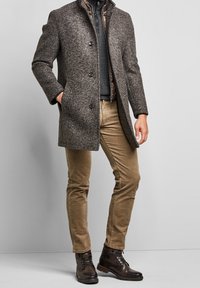Cappotto da uomo in misto lana grigio con colletto a risvolto, chiusura con bottoni e tasche laterali, abbinato a pantaloni khaki e stivali in pelle marrone.
