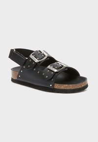 Svart lädersandal med två metallspännen, öppen tå och korkliknande sula. Har silvernitar längs spännena och en slingback-design.