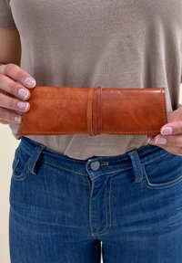 Brūns ādas maks, pagarināta taisnstūra forma, gluda virsma, nodrošināta ar ādas siksnu, ar kontrastējošām šuvju detaļām.