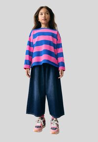 Långärmad, lös passform topp med blå och rosa horisontella ränder, i kombination med vida mörk denimbyxor och rosa sneakers med leopardmönster.