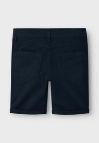 Shorts bleu foncé avec un ourlet roulé, deux poches arrière avec des bords surpiqués et une texture lisse semblable à du coton.