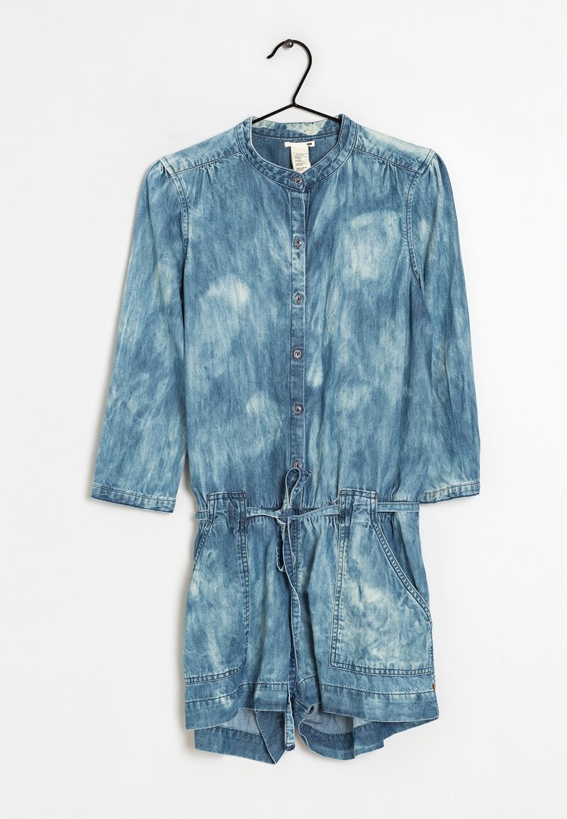 Salopette en denim à manches longues, devant boutonné, délavage bleu clair, taille à cordon, et deux poches avant. Tissu doux et texturé avec des zones décolorées.