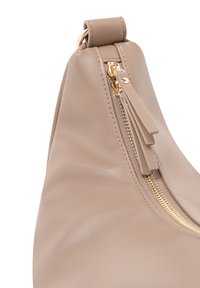 Béžová kožená kabelka s elegantním, zakřiveným designem. Obsahuje zlatý zip, texturovaný povrch a kožené táhla. Minimalistická estetika.