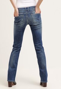 Denimjeans i ett blekt mörkblått utförande, med smal passform, två bakfickor och synlig sömnad, visade från baksidan.
