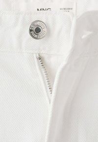 Primer plano de pantalones de mezclilla blancos que muestran un botón plateado grabado con "DENIM MNG AUTHENTIC" y una cremallera metálica parcialmente cerrada.