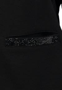 Black fabric featuring a horizontal pocket adorned with a row of small silver studs, offering a textured contrast against the smooth material.