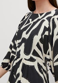 Robe noire et crème avec des manches courtes surdimensionnées, un col rond et un motif abstrait. Le tissu est léger avec une texture douce.