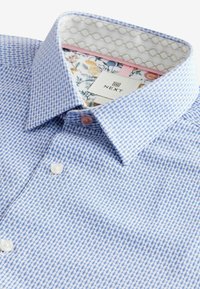 Camicia blu a fantasia con design geometrico, apertura con bottoni e colletto foderato a fiori in contrasto con etichetta del marchio. Tessuto strutturato.