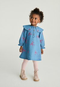 Denimkjole med stor krave, rosa broderede sløjfer og knaplukning foran. Hvide kabelstrik strømpebukser og beige snørebodder fuldender outfittet.