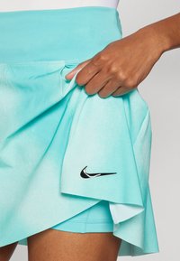 Egy könnyű anyagból készült türkiz színű sportszoknya, fekete Nike logóval, belső réteggel a kényelmesebb illeszkedés és a jobb takarás érdekében.