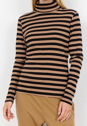 Femme portant un col roulé ajusté à manches longues avec des rayures horizontales noires et marron, associée à un pantalon couleur chameau.