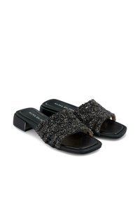 Mule neri aperti sulla punta con un intricata tomaia in perline. Tacco quadrato, soletta in pelle liscia e una fascia decorata e texture.