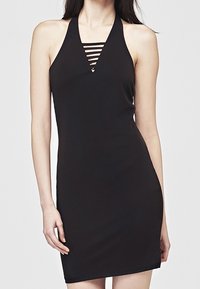 Femme portant une robe noire cintrée sans manches avec un col licou et des détails de bandes horizontales au niveau de la poitrine.