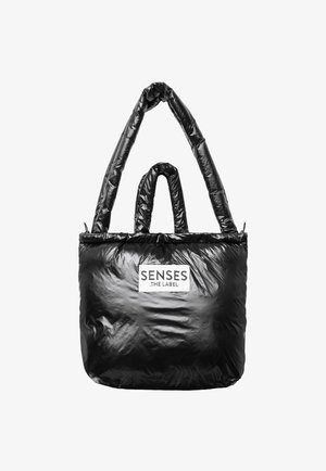 Black tote bag made from glossy material, featuring two handles and a logo patch. The design is spacious with a soft, smooth texture.