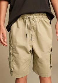 Khaki cargo shorts med elastisk talje og snor. Har sidelommer og en løs pasform med en glat stofstruktur.