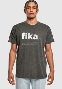 Sötét szürke, rövid ujjú póló, nagy fehér betűkkel „fika” felirattal, alatta kisebb betűmérettel a definícióval. Puha anyag, laza szabás.