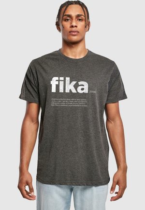 Mørkegrå T-shirt med korte ærmer, der har "fika" i store hvide bogstaver, med en definition trykt nedenfor i mindre skrifttype. Blødt stof, afslappet pasform.