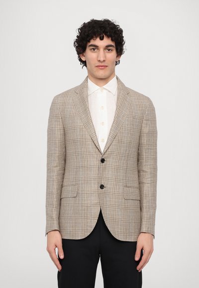 Beige ternetternet blazer med notched lapel, to forlommer og to sorte knapper. Båret over en hvid skjorte og parret med sorte bukser.