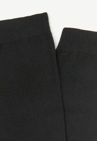 Schwarze Socken aus weichem, dehnbarem Stoff mit einer glatten Textur und einem schlichten, nahtlosen Design. Jede Socke hat eine abgerundete obere Kante.