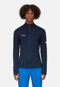 Marineblaue Zip-Up-Jacke mit strukturierter Oberfläche, ausgestattet mit einer Brusttasche, hohem Kragen und orangefarbenem Reißverschlussakzent. Logo auf der linken Seite.
