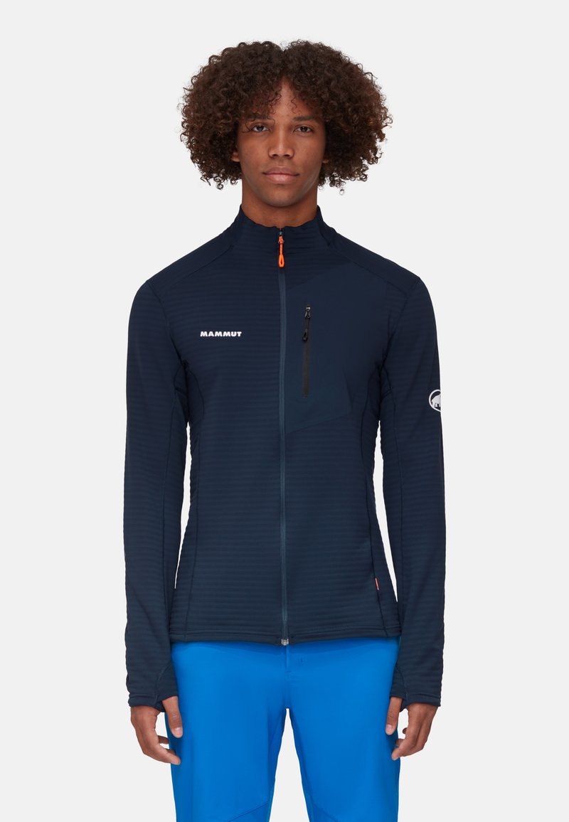 Marineblaue Zip-Up-Jacke mit strukturierter Oberfläche, ausgestattet mit einer Brusttasche, hohem Kragen und orangefarbenem Reißverschlussakzent. Logo auf der linken Seite.