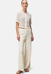 Giacca in pizzo a maniche corte con bottoni, abbinata a pantaloni larghi in pizzo con un motivo dettagliato in off-white. Sandali piatti completano il look.
