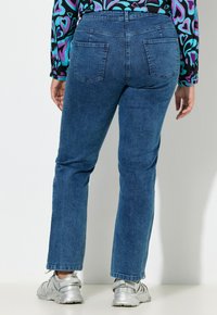 Jeans in denim blu scuro con taglio a gamba dritta, dotati di due tasche posteriori e vita a metà altezza. Indossati con scarpe sportive argentate.