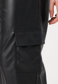 Zwarte neplederen cargo broek met een zijzak, een gladde textuur en een getailleerde pasvorm. Het materiaal weerkaatst het licht subtiel.