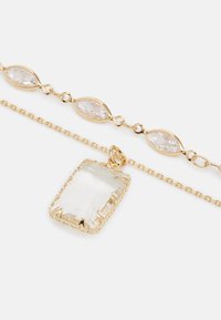 Collier doré mettant en avant un pendentif en pierre claire de forme rectangulaire et des charms ovales liés, présentant une finition polie et un design de chaîne délicat.