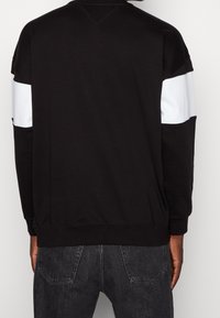 Sudadera negra con franjas blancas horizontales en los hombros, hecha de una suave mezcla de algodón con puños y cintura acanalados.