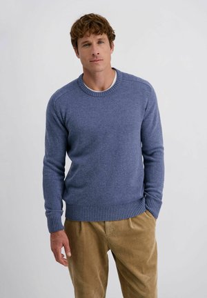 Crewneck sweater in zachtblauwe brei, met ribboorden aan de mouw- en onderkant. Gecombineerd met beige corduroy broek voor een textuurrijke tegenstelling.