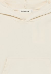 Φούτερ με κουκούλα σε κρεμ απόχρωση, διαθέτει μπροστινή τσέπη, κορδόνι στην κουκούλα και υφασμάτινη ετικέτα με την επιγραφή "BILLIEBLUSH" στο λαιμό. Μαλακή υφή.