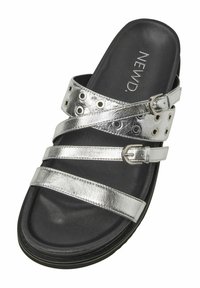 Silverfärgade metalliska sandaler med flera korsade remmar och spännare, med en strukturerad svart innersula och gummiyttersula.