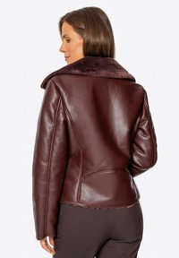 Burgundowa skórzana kurtka z pluszowym, ciemnym futrem przy kołnierzu. Posiada dopasowany krój oraz gładką fakturę. Wyróżniające się szwy z tyłu i boczne kieszenie.