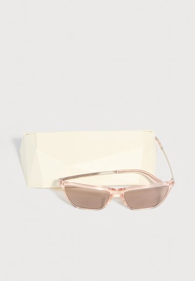 Ροζ διαφανή γυαλιά ηλίου σε στυλ «μάτια γάτας» με καφετί φακούς, τοποθετημένα μπροστά από μια μπεζ σκληρή θήκη σε λευκό φόντο.