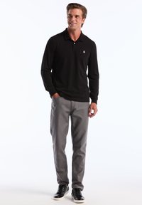 Zwarte langemouwen polo met een klein logo, gecombineerd met slim-fit grijze broeken en zwarte sneakers met witte zolen.