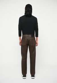 Rjave traperice s ravnim krojem, z dvema zadnjima žepoma in visokim pasom. Stilizirane s črno majico dolgimi rokavi.