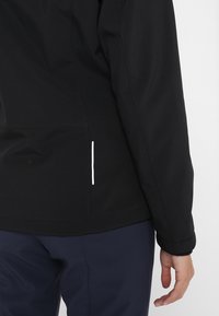 Veste noire au design élégant, avec une poche latérale accentuée de blanc. Texture lisse et col haut pour la chaleur.