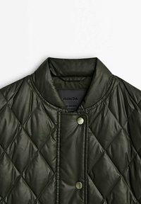 Kurtka pikowana w kolorze zielonym z wysokim kołnierzem, z zapięciem na napy i gładką, błyszczącą fakturą. Metka widoczna wewnątrz dekoltu.