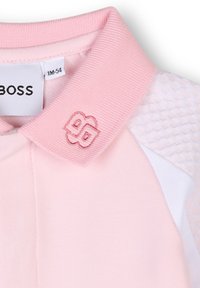 Polo en tissu rose doux avec col côtelé. Présente des panneaux latéraux blancs et des accents texturés sur les épaules. Logo BOSS en broderie rose.