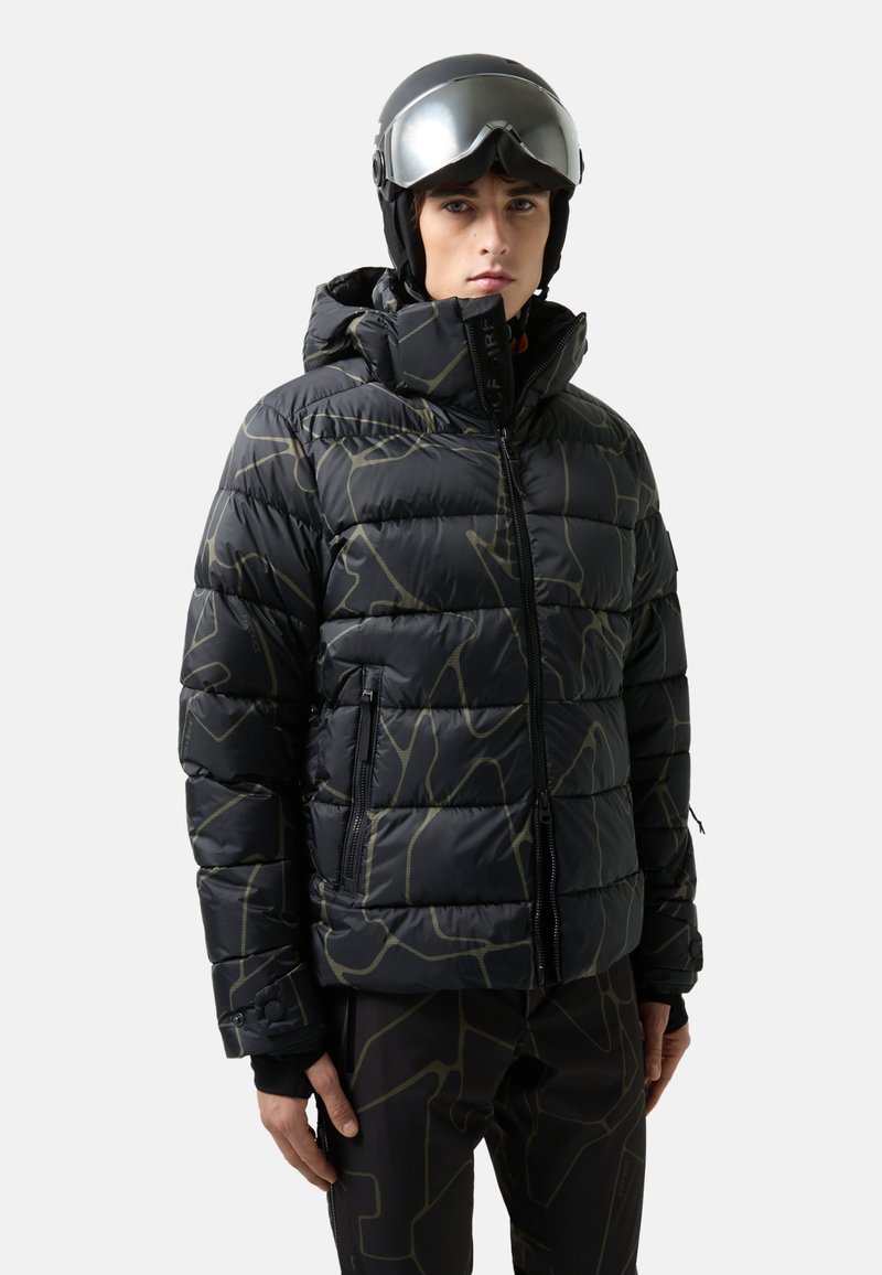 Schwarze Pufferjacke mit geometrischem olivgrünem Muster, Kapuze, Reißverschlusstaschen und elastischen Bündchen, getragen mit schwarzen Skihosen und Skibrille.