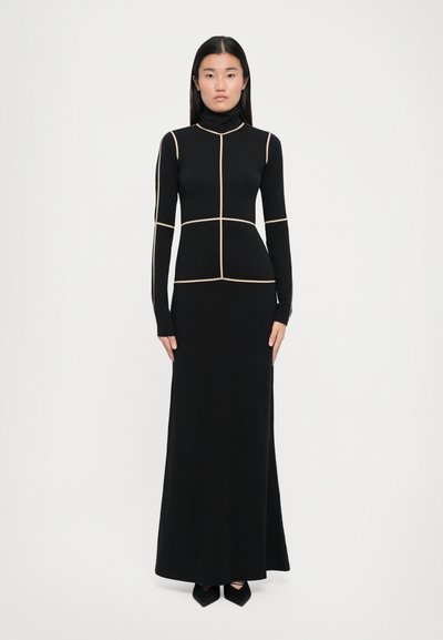 Robe noire à manches longues en tissu extensible, présentant un col haut et des coutures géométriques de couleur crème qui soulignent la silhouette.