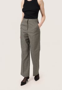 Pantaloni a gamba larga in un tessuto grigio testurizzato, caratterizzati da una vita alta e tasche laterali. Abbinati a una canotta nera e tacchi neri.