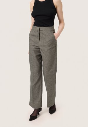 Hoch taillierte weite Hosen aus einem strukturierten grauen Stoff, mit seitlichen Taschen. Kombiniert mit einem schwarzen Tanktop und schwarzen High Heels.