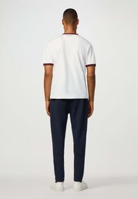 Biela polo košeľa s vínovými kosticami na rukávoch; námornícke nohavice. Model stojí chrbtom k divákovi. Jednoduchý dizajn, voľný strih a jednofarebné farby.