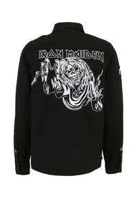 Fekete póló, nagy fehér grafikával a hátsó oldalon, amely egy csontváz alakot és az "IRON MAIDEN" szöveget ábrázol. Hosszú ujjú, gombokkal.