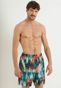 Costumi da bagno colorati con un motivo astratto multicolore, dotati di un elastico in vita e di un cordoncino arancione a contrasto.