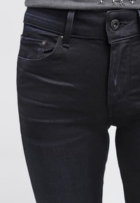 Mörkblå jeans med slim fit, som har en medelhög midja, femficksdesign och en subtil lyster på denimtyget. Metallknappstängning.